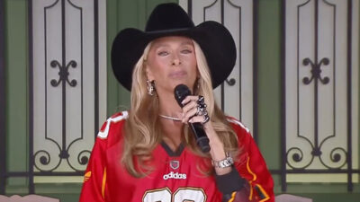 Adriane Galisteu usa chapéu preto e camisa vermelha enquanto apresenta A Fazenda 17 segurando microfone