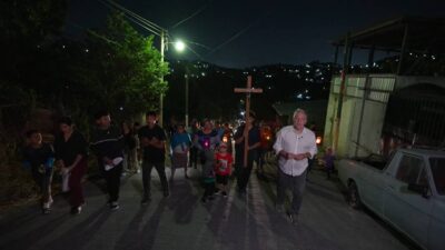 Álvaro Pereira Junior caminha ao lado de moradores durante procissão noturna em rua iluminada por postes em El Salvador