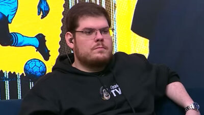 Casimiro Miguel sentado em estúdio da CazéTV usando moletom preto com logotipo do canal e fone de ouvido