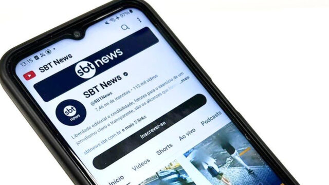 Celular exibindo a página do canal SBT News no YouTube com logotipo, botão inscrever-se e vídeos em destaque