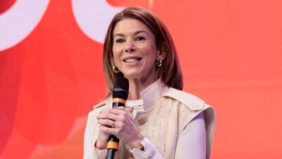 Daniela Abravanel Beyruti presidente do SBT fala sorrindo ao microfone em evento com fundo vermelho