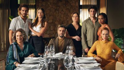Elenco principal da novela Mania de Você reunido em torno de mesa de jantar posta com taças e pratos em ambiente sofisticado