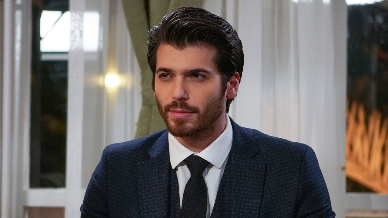 Can Yaman caracterizado como Ferit Aslan veste terno escuro e gravata em cena da novela turca Dolunay