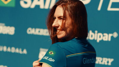 Glenda Kozlowski sorri de lado vestindo camisa do Mubadala Brazil SailGP Team com bandeira do Brasil e nome Glenda na manga