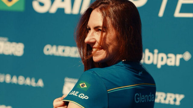 Glenda Kozlowski sorri de lado vestindo camisa do Mubadala Brazil SailGP Team com bandeira do Brasil e nome Glenda na manga