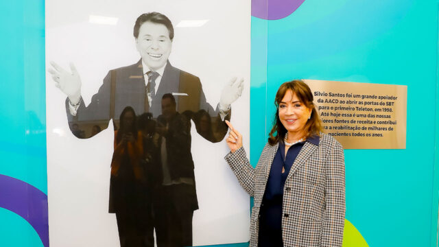 Iris Abravanel sorri ao lado de painel com foto de Silvio Santos durante homenagem ao apresentador na sede da AACD em São Paulo