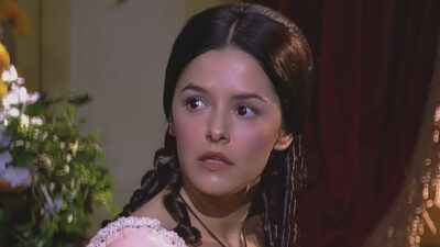 Isaura interpretada por Bianca Rinaldi usa vestido de época claro e colar com crucifixo em cena da novela A Escrava Isaura olhando assustada para o lado