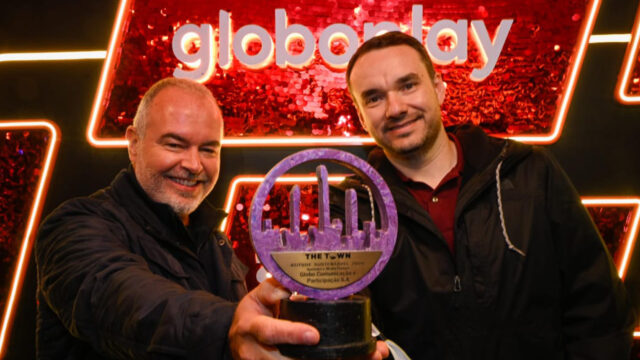 Pedro Secchin e Thiago Martins sorrindo e exibindo troféu do prêmio The Town em frente a painel vermelho com logotipo Globoplay