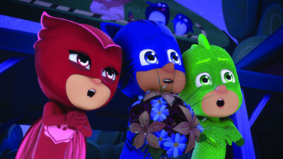 Personagens Corujita, Menino-Gato e Lagartixo de PJ Masks observam algo assustados enquanto seguram um buquê de flores