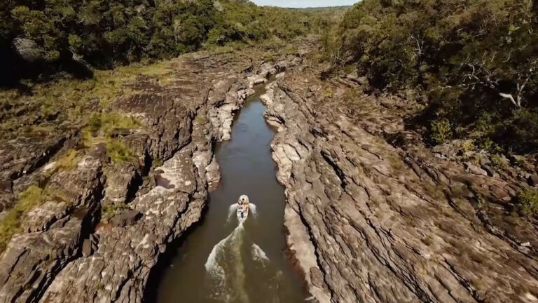 Barco com pessoas navegando por rio estreito entre paredões de pedra cercados por vegetação no documentário Raízes do Araguaia