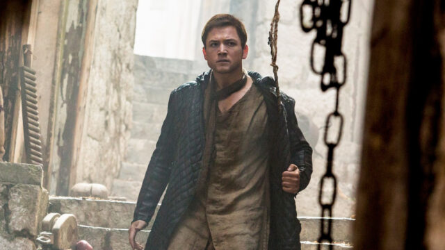 Taron Egerton caracterizado como Robin Hood usando roupas escuras em cena de Robin Hood: A Origem, de 2018