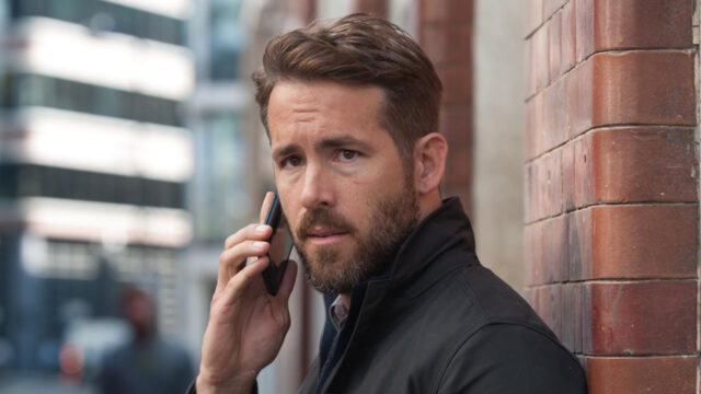 Ryan Reynolds caracterizado como Bill Pope fala ao celular encostado em parede de tijolos em cena do filme Mente Criminosa 2016