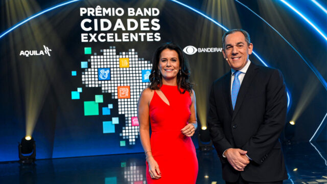 Adriana Araújo e Marco Antonio Sabino no palco do Prêmio Band Cidades Excelentes com telão iluminado ao fundo