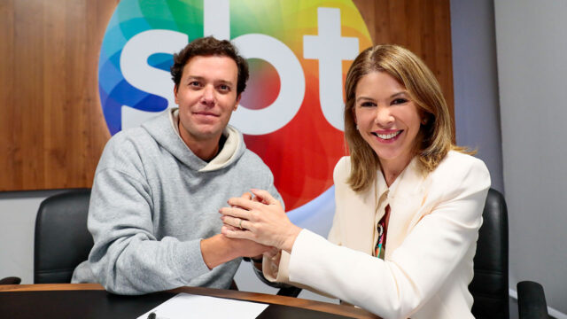 André Valadão, de moletom cinza, e Daniela Abravanel Beyruti, de blazer claro, dão as mãos em sala de reunião na sede do SBT