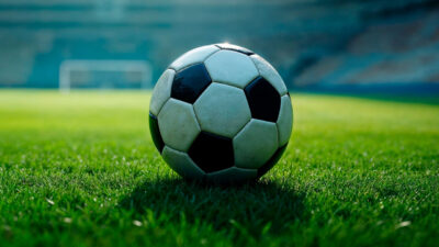 Bola de futebol clássica em close-up no centro do gramado verde de um estádio, pronta para o início de um jogo transmitido pela TV