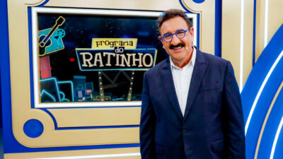 Carlos Massa, o Ratinho, sorri no estúdio do Programa do Ratinho com logotipo exibido ao fundo