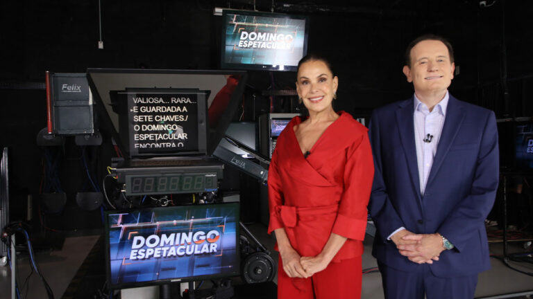 Carolina Ferraz, de roupa vermelha, e Roberto Cabrini, de terno azul, posam no estúdio do Domingo Espetacular na Record