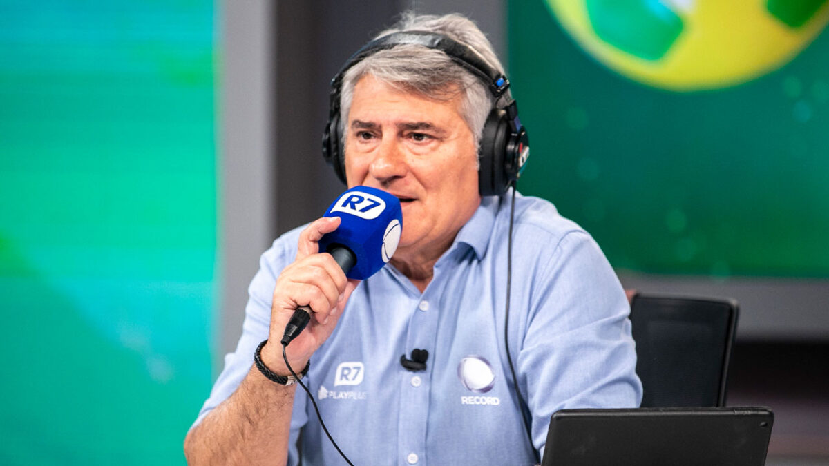 Cléber Machado com fones de ouvido e microfone com espuma azul durante transmissão esportiva da Record