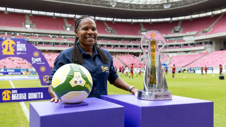 Formiga sorri ao lado da taça e da bola da Copa Maria Bonita em campo de estádio com arquibancadas ao fundo