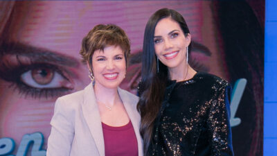 Glória Vanique e Daniela Albuquerque sorrindo no estúdio do programa Sensacional com telão ao fundo