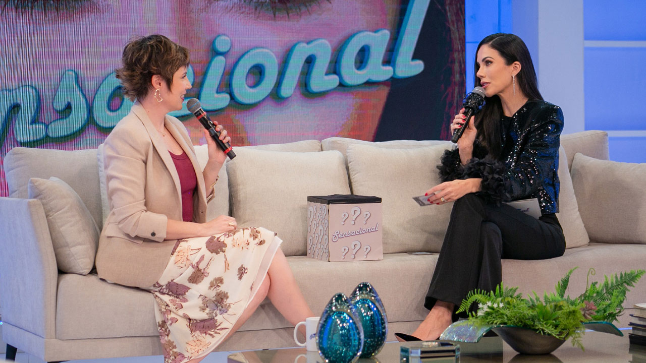Glória Vanique e Daniela Albuquerque conversam com microfones no sofá do programa Sensacional na RedeTV