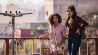 Joélly (Alana Cabral) com jaqueta rosa e Gerluce (Sophie Charlotte) de blusa vinho, paradas em um viaduto em cena de Três Graças