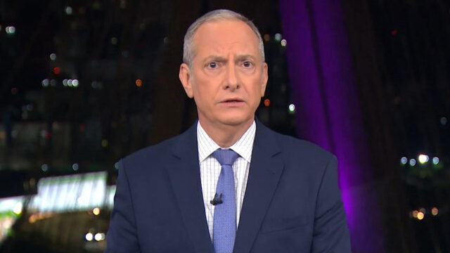 O jornalista José Roberto Burnier, de terno azul e gravata, apresenta o telejornal SP2 no estúdio de vidro da Globo com cenário noturno