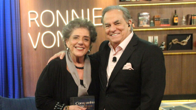 Leda Nagle e o apresentador Ronnie Von sorriem abraçados no estúdio do Companhia Certa, com o logo do programa ao fundo