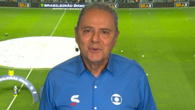 Luis Roberto com camisa azul da Globo e microfone de lapela durante transmissão do Brasileirão em estádio de futebol