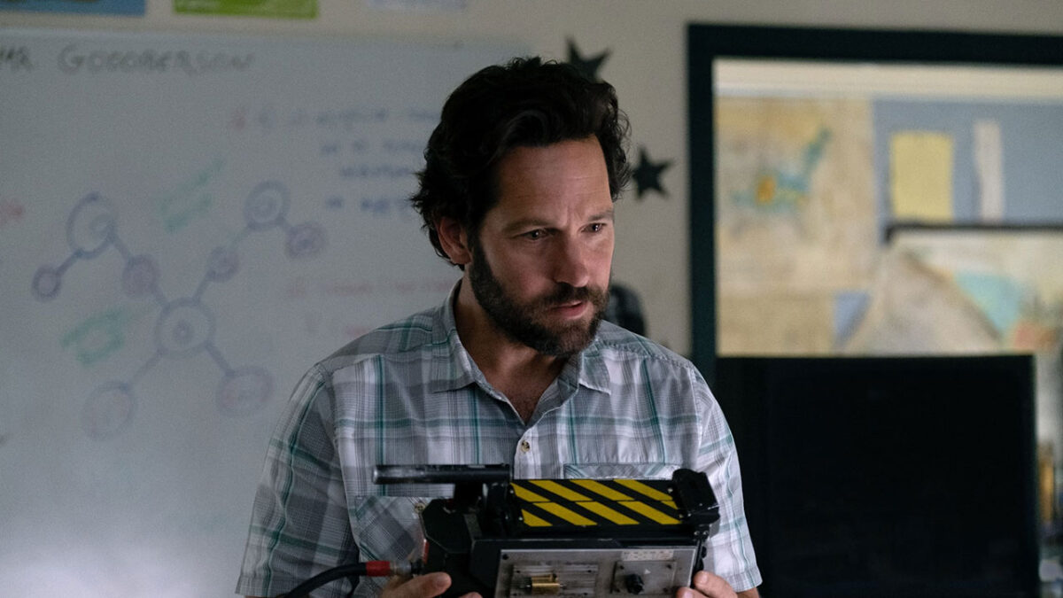Paul Rudd como Grooberson, de camisa xadrez, segura uma armadilha de fantasma em sala de aula em cena de Ghostbusters: Mais Além