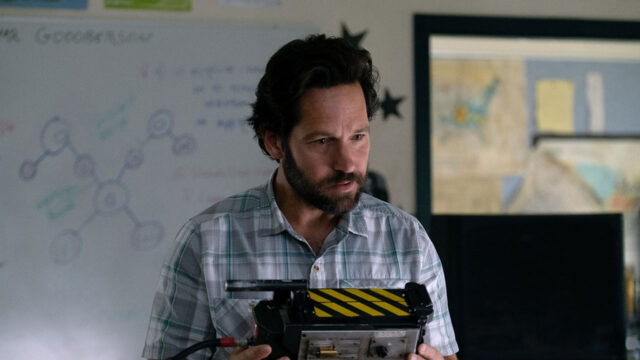 Paul Rudd como Grooberson, de camisa xadrez, segura uma armadilha de fantasma em sala de aula em cena de Ghostbusters: Mais Além