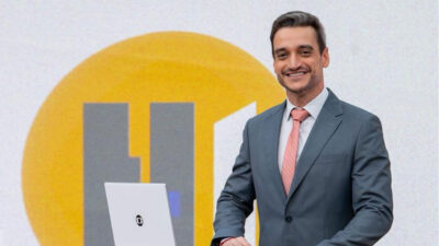 Tiago Scheuer de terno cinza e gravata rosa apresentando o telejornal Hora 1 da TV Globo