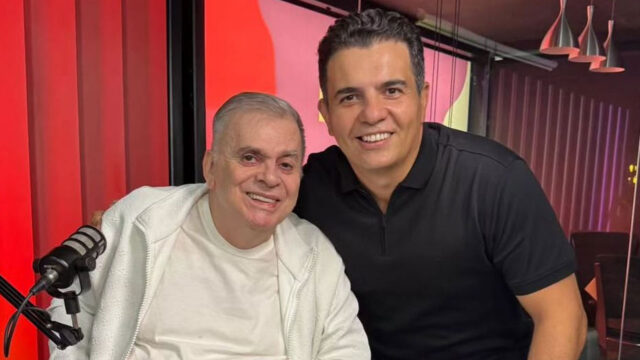 Walcyr Carrasco e Anderson Cavalcante sorrindo lado a lado em estúdio com microfone e fundo vermelho iluminado
