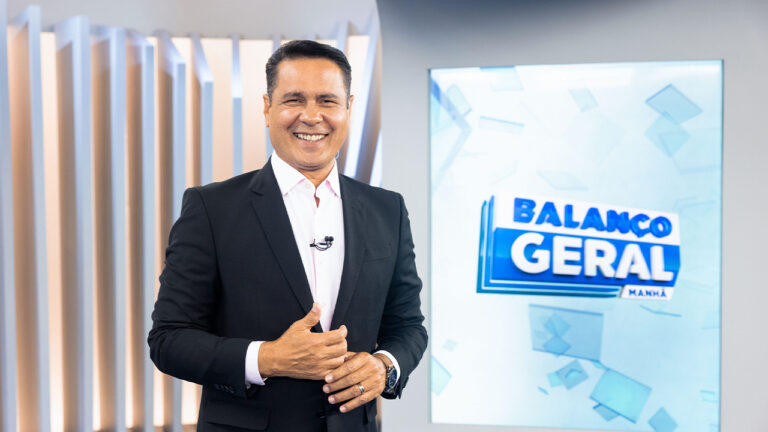 Willian Leite sorrindo no estúdio do Balanço Geral Manhã SP com telão do programa ao fundo
