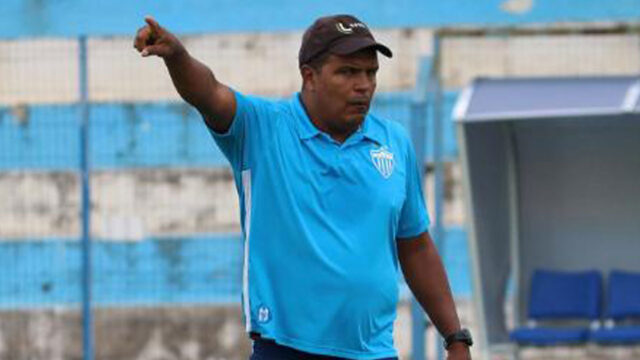 O ex-zagueiro Alexandre Lopes, com boné e camisa azul, gesticula com o braço apontado durante partida de futebol no campo
