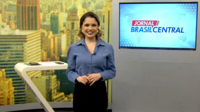 Apresentadora Danuza Azevedo sorrindo no estúdio do Jornal Brasil Central com monitor de LED exibindo o nome do telejornal