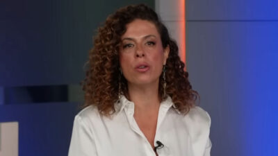 Fabíola Cidral, jornalista com cabelo cacheado, apresentando o UOL News vestindo uma camisa social branca