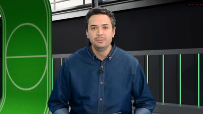 Apresentador Felipe Melo Tonelli, de camisa jeans azul escura, no estúdio da Xsports com fundo preto e detalhes em verde