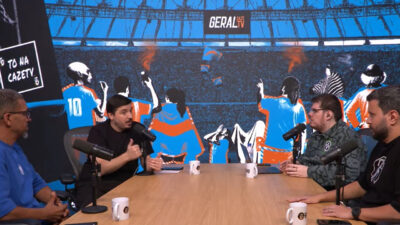 Casimiro e outros apresentadores da CazéTV sentados ao redor da mesa em estúdio com tema de estádio