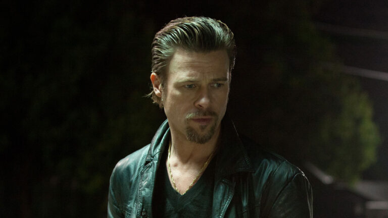 Ator Brad Pitt como Jackie com cabelo penteado para trás e jaqueta de couro em cena do filme O Homem da Máfia de 2012