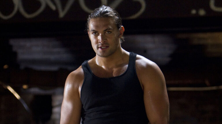 Jason Momoa como Keegan usando regata preta, olhando fixamente para a câmera em cena do filme Alvo Duplo