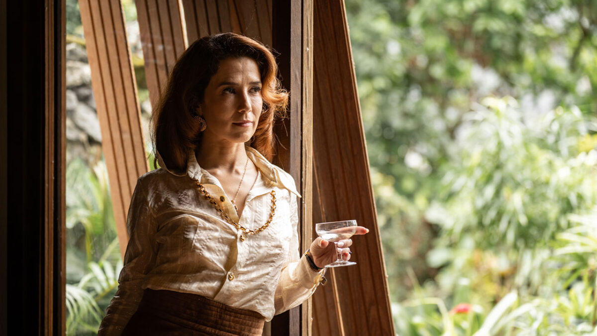 Marjorie Estiano como Ângela Diniz, de camisa de seda e colar dourado, segura taça de bebida em cena de série da HBO Max