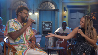 Nego Álvaro e Teresa Cristina cantando e sorrindo em estúdio que simula um bar carioca no programa Samba na Gamboa