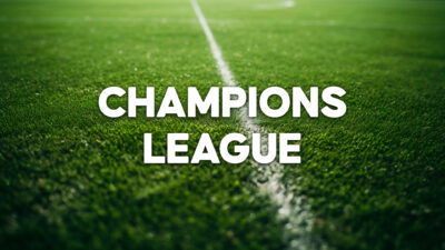 Nome Champions League escrito em letras brancas na grama verde de um campo de futebol com linha central demarcada