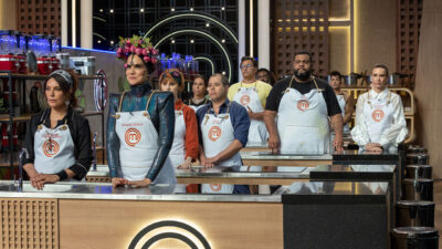 Participantes do MasterChef Celebridades alinhados na bancada de cozinha no estúdio