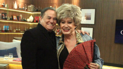 Ronnie Von de preto e Nany People com jaqueta jeans e peruca loira, sorrindo e abraçados no programa Companhia Certa