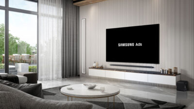 Smart TV da Samsung em uma sala de estar moderna exibindo o logotipo da Samsung Ads em branco na tela preta