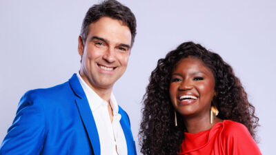 Tadeu Schmidt de blazer azul e Kenya Sade de blusa vermelha com brinco dourado posam sorrindo para a câmera