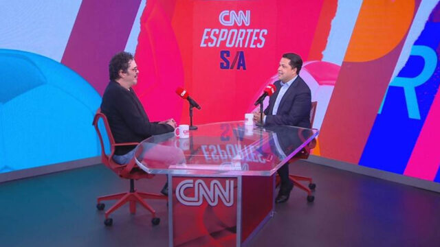 Walter Casagrande e João Vitor Xavier sentados em bancada de vidro com microfones no estúdio do CNN Esportes S/A