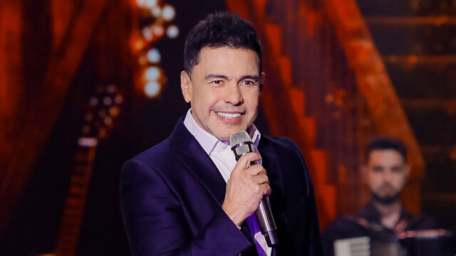 Cantor Zezé Di Camargo sorrindo no palco segurando o microfone, durante a gravação do especial Natal é Amor no SBT